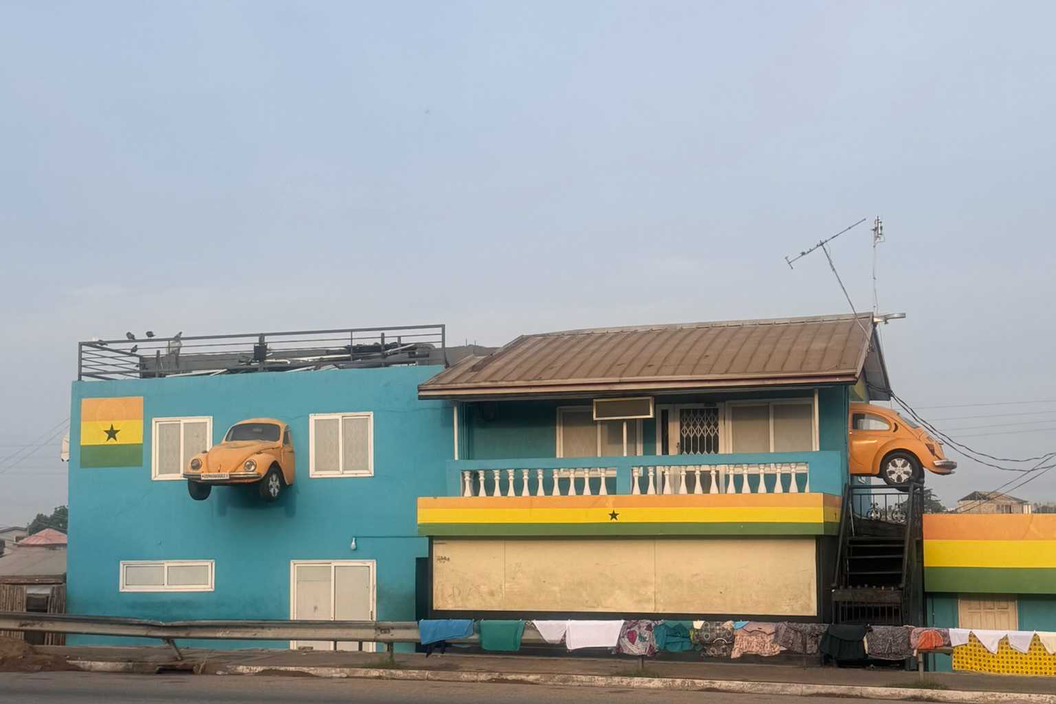 A teal house in Accra with a yellow Volkswagen Beetle mounted on the wall